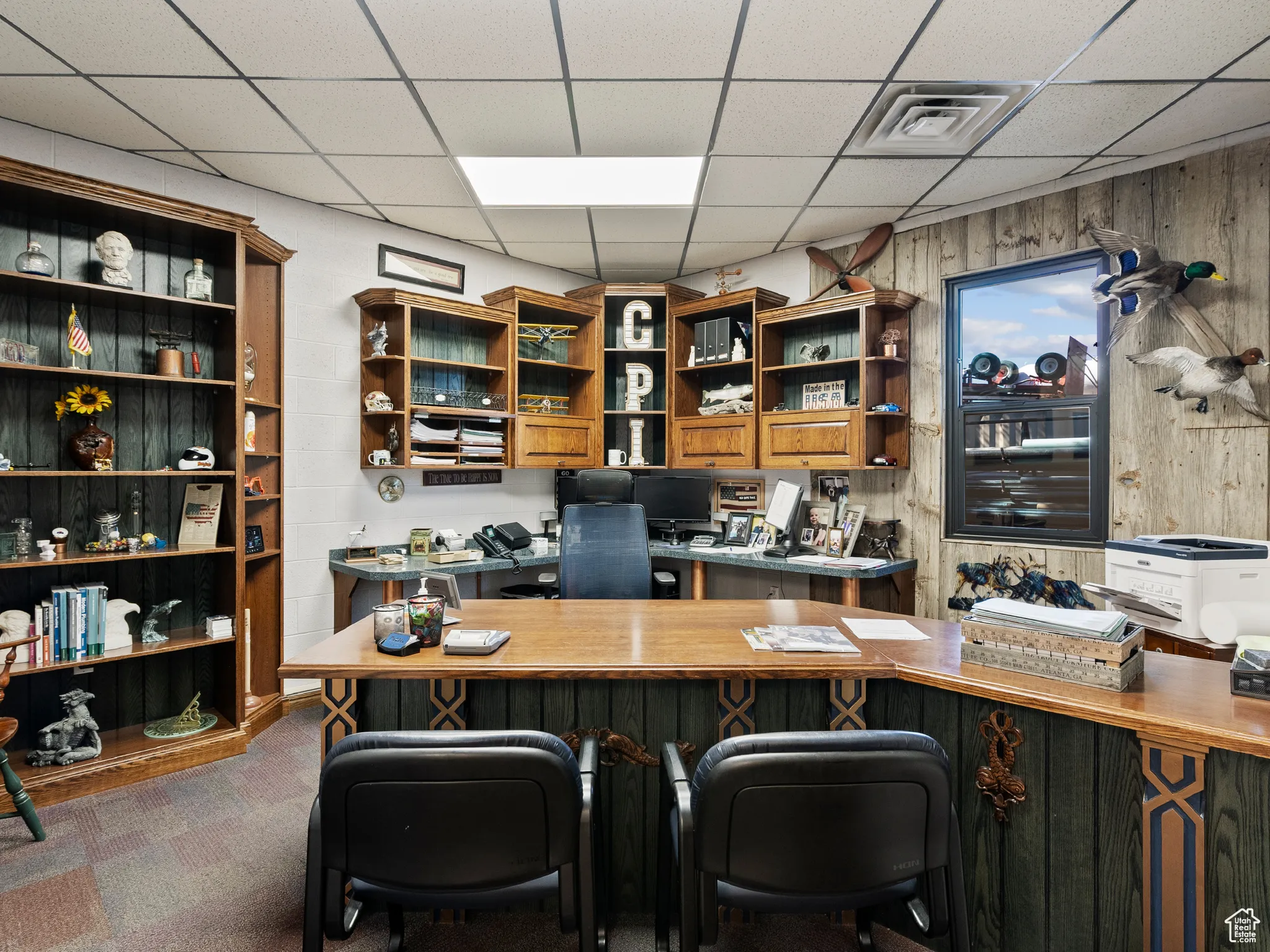 Office with a drop ceiling, wood walls, and dark colored carpet