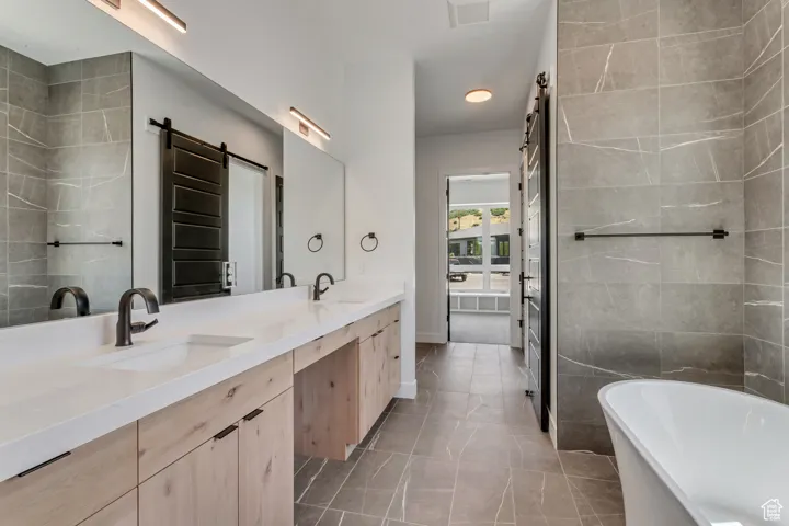 Primary bathroom featuring double vanity, a soaking tub, light tile patterned floors, and tile walls