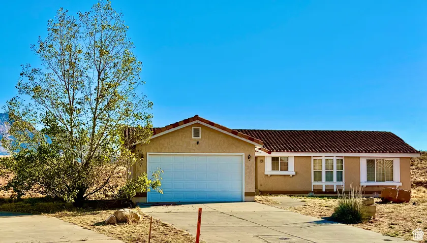 View of front of property featuring concrete driveway, stucco siding, a tiled roof, and an attached garage