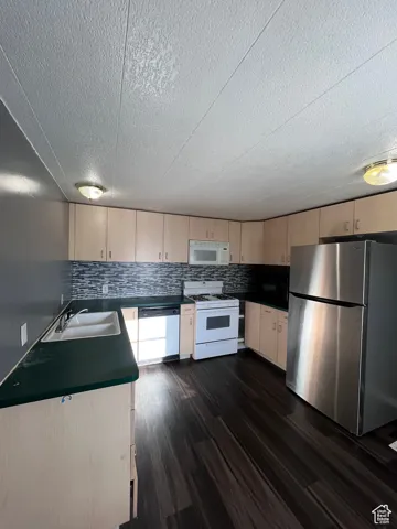 Kitchen featuring appliances with stainless steel finishes, dark wood-style flooring, dark countertops, decorative backsplash, and a textured ceiling