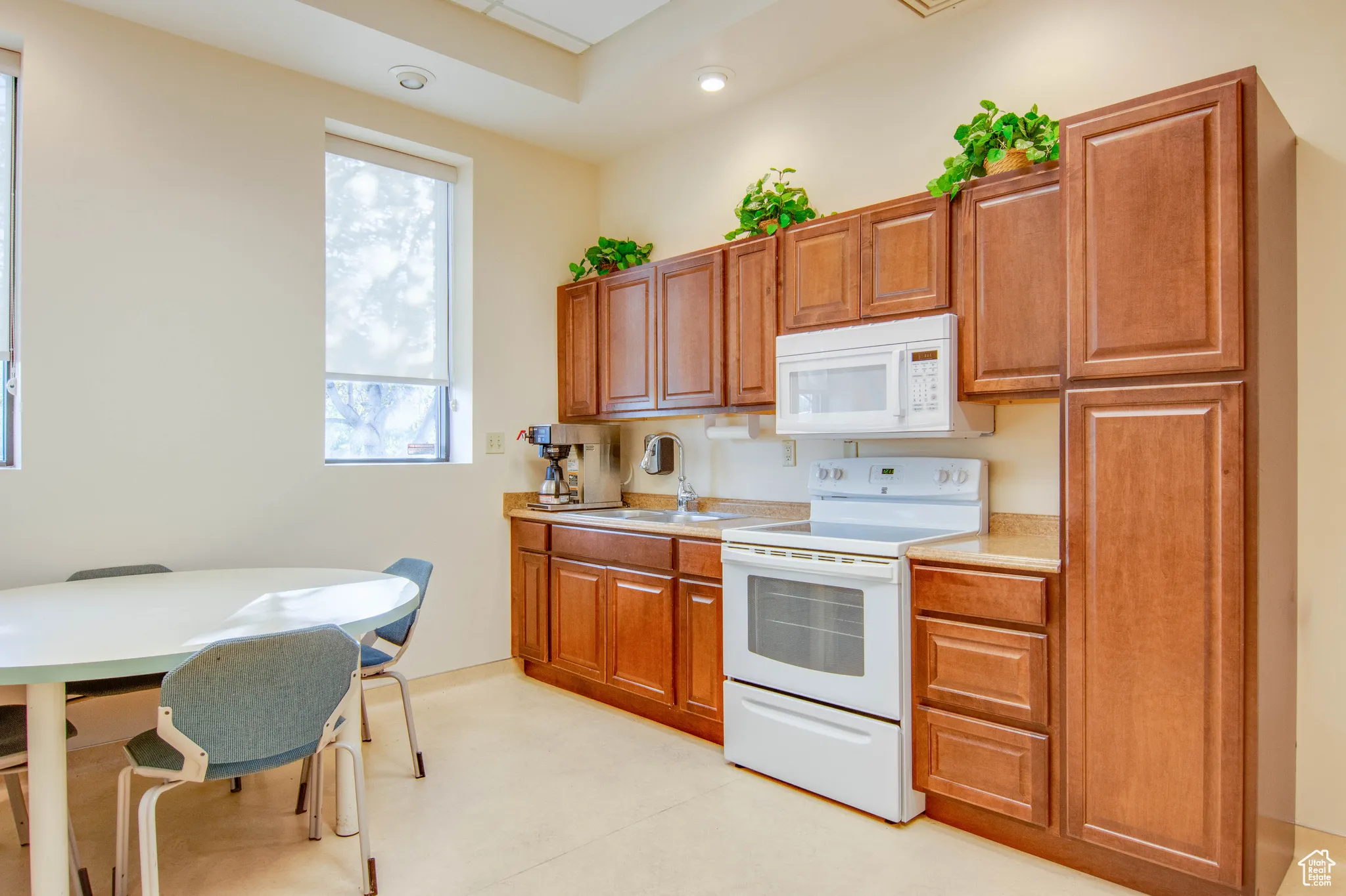 Kitchen with white appliances, light countertops, brown cabinetry, and recessed lighting