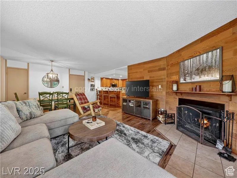Living area featuring wood walls, a textured ceiling, a warm lit fireplace, and wood finished floors