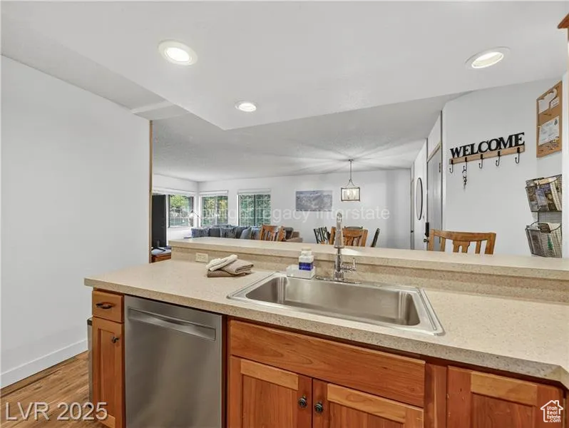 Kitchen featuring stainless steel dishwasher, brown cabinets, light wood-style floors, open floor plan, and recessed lighting