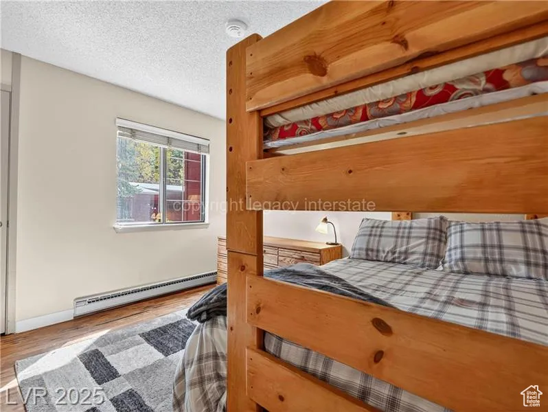 Bedroom featuring wood finished floors, a baseboard radiator, and a textured ceiling