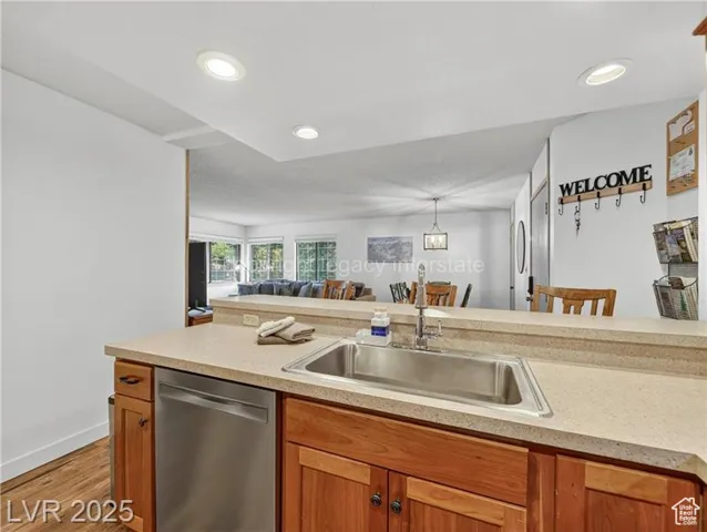 Kitchen featuring stainless steel dishwasher, brown cabinets, light wood-style floors, open floor plan, and recessed lighting