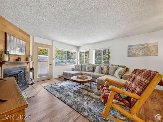 Living room with a fireplace with flush hearth, a textured ceiling, and wood finished floors