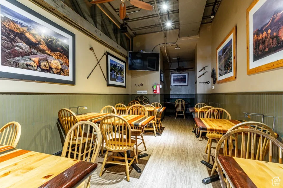 Dining space featuring ceiling fan, wood finished floors, wainscoting, and a towering ceiling