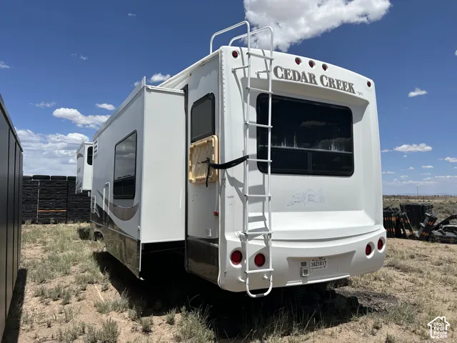 White "Cedar Creek" RV with a rear ladder, multiple windows, and a brown and black accent stripe
