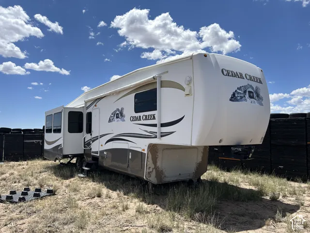 Fifth wheel Cedar Creek recreational vehicle featuring an awning, multiple exterior windows, an entry door with steps, and a white and brown exterior finish