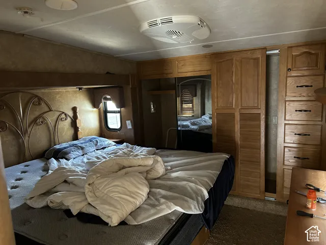 Bedroom featuring a decorative headboard, integrated bedside shelf, wood-finish cabinetry, mirrored closet doors, and recessed lighting