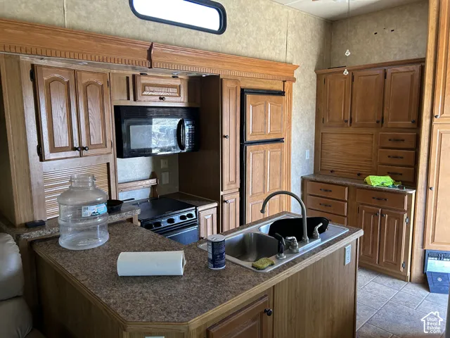 Kitchen featuring wood-finish cabinetry, a stainless steel double basin sink, and a black microwave