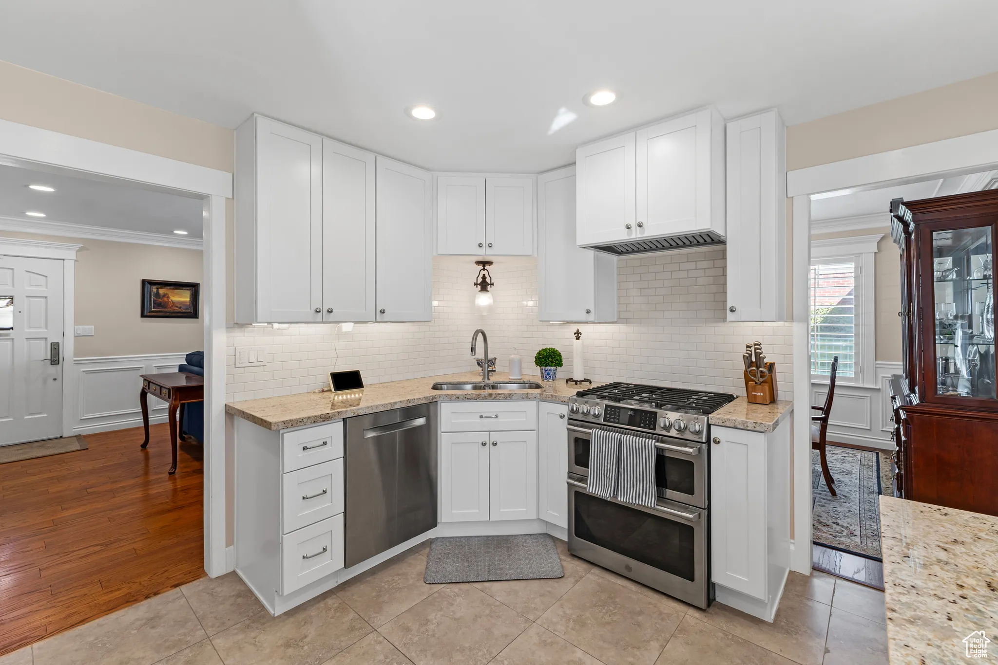 Kitchen with appliances with stainless steel finishes, ornamental molding, white cabinets, light stone countertops, and recessed lighting