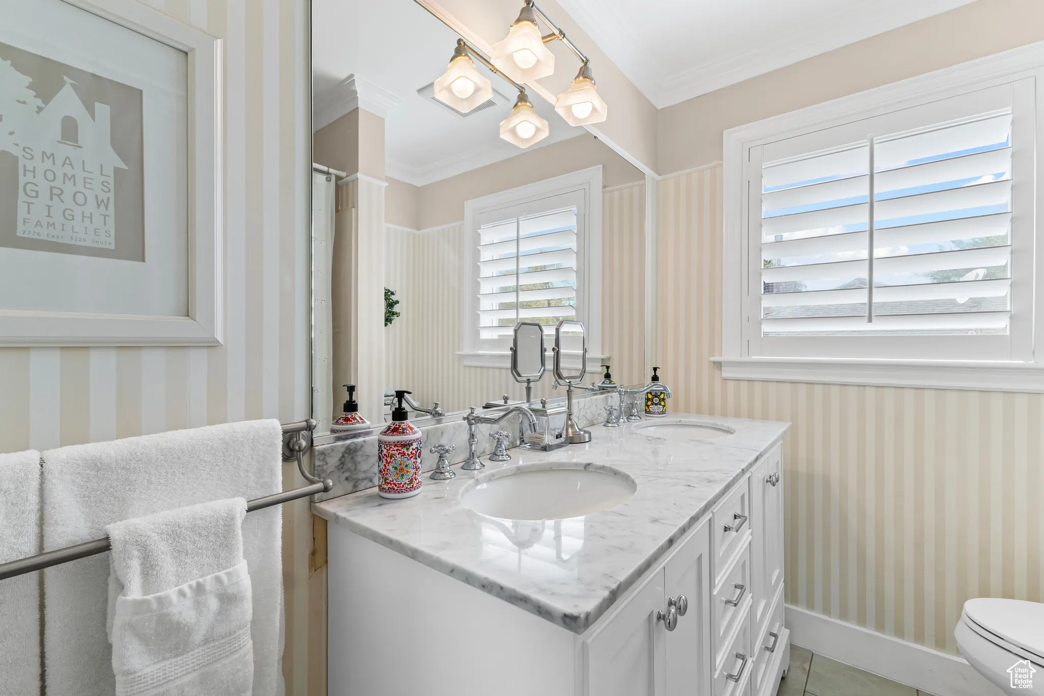 Bathroom featuring wallpapered walls, double vanity, ornamental molding, a chandelier, and light tile patterned flooring