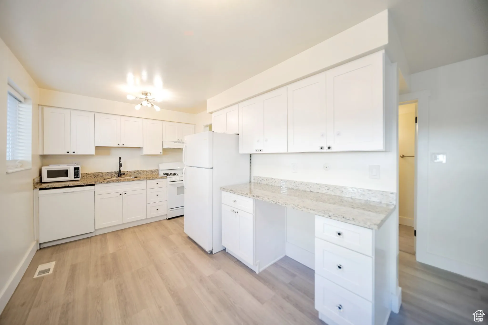 Kitchen with white cabinets, white appliances, light wood-style floors, light stone countertops, and under cabinet range hood