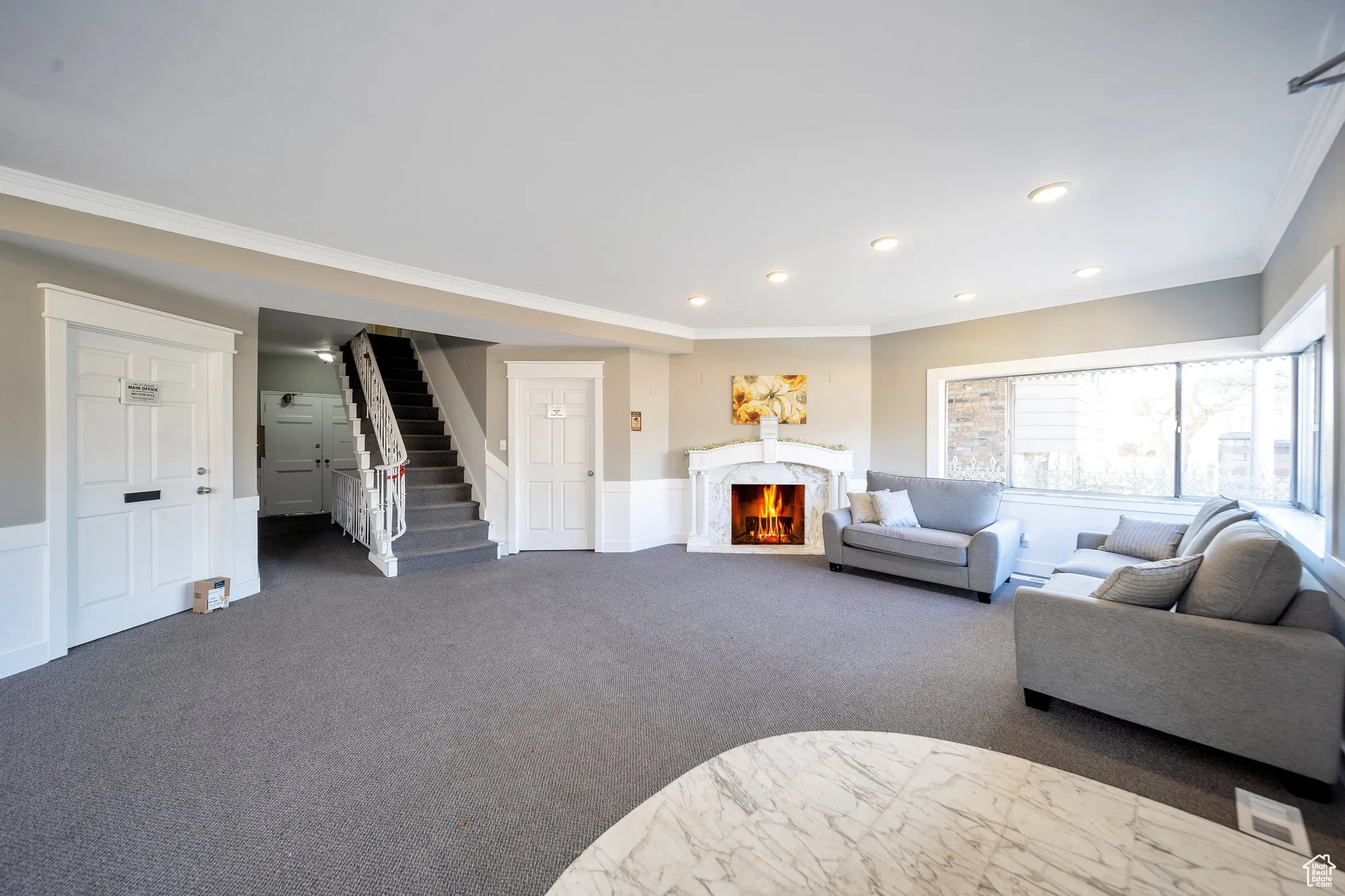Carpeted living room featuring ornamental molding, a fireplace, a wainscoted wall, stairway, and recessed lighting