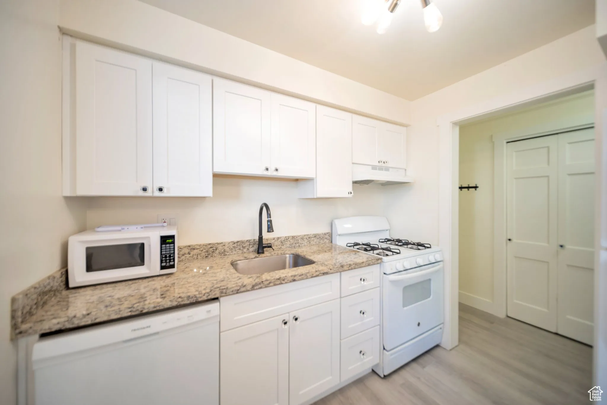 Kitchen with white appliances, white cabinetry, light wood-style floors, light stone counters, and under cabinet range hood