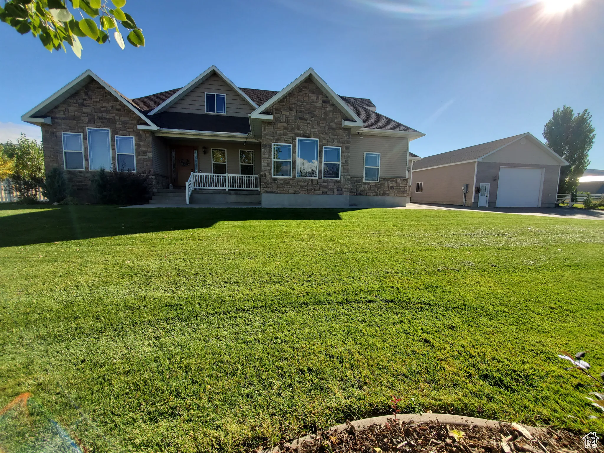 Craftsman house with stone siding, covered porch, a front lawn, and an outdoor structure