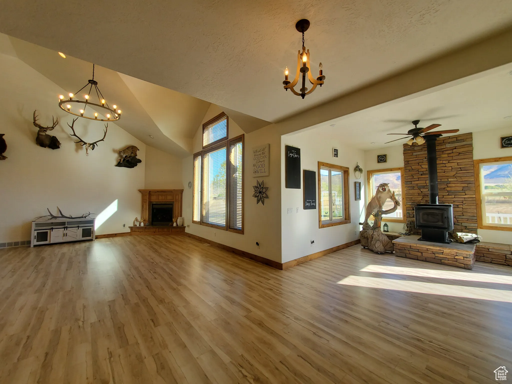 Unfurnished living room featuring a chandelier, wood finished floors, a fireplace, a wood stove, and lofted ceiling