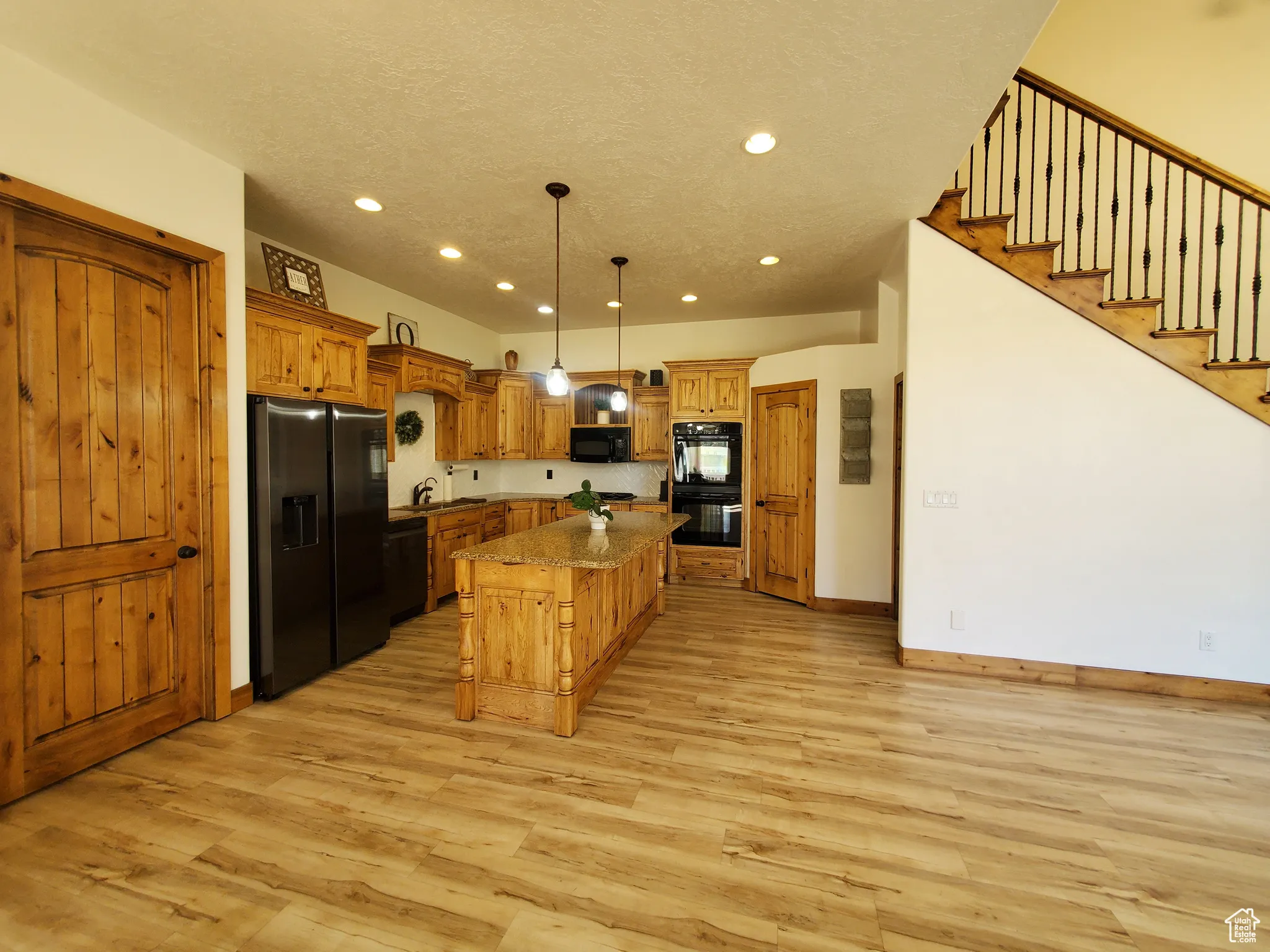Kitchen with black appliances, decorative light fixtures, a breakfast bar, a kitchen island, and light wood-style flooring