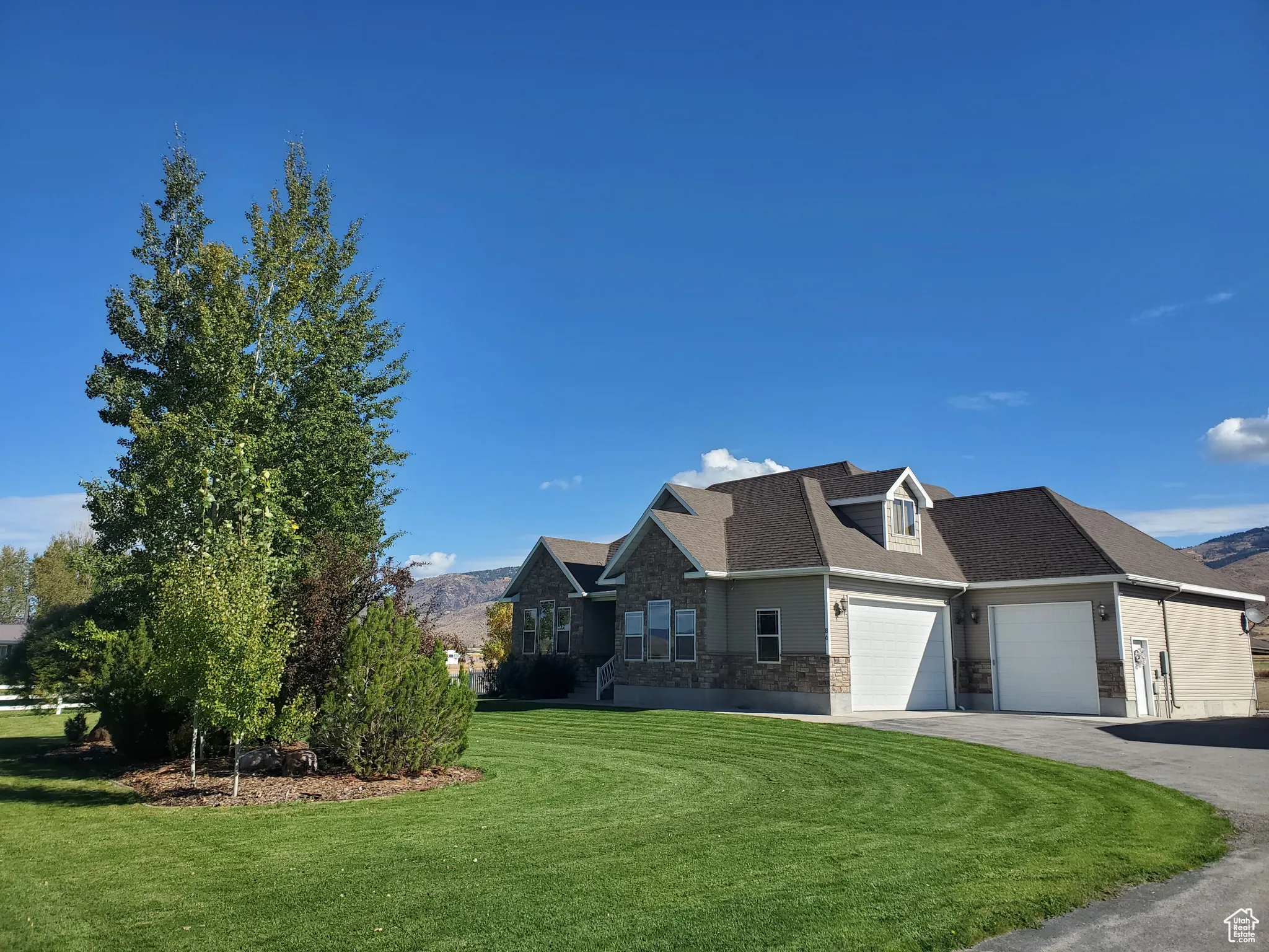 View of front of property with stone siding, a front lawn, asphalt driveway, a mountain view, and a shingled roof