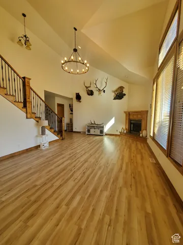 Unfurnished living room featuring stairs, a fireplace with raised hearth, high vaulted ceiling, light wood finished floors, and a chandelier