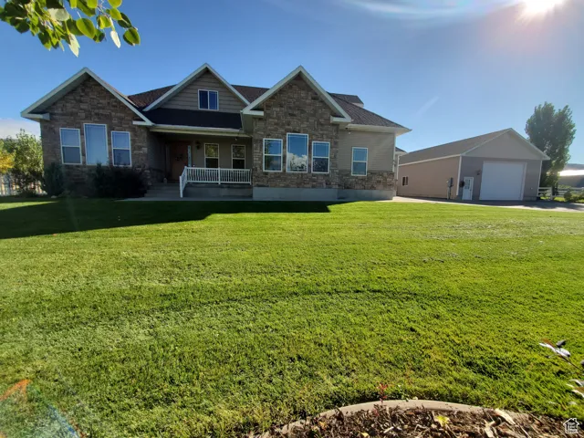 Craftsman house with stone siding, covered porch, a front lawn, and an outdoor structure