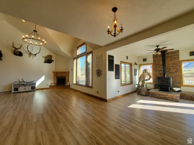 Unfurnished living room featuring a chandelier, wood finished floors, a fireplace, a wood stove, and lofted ceiling