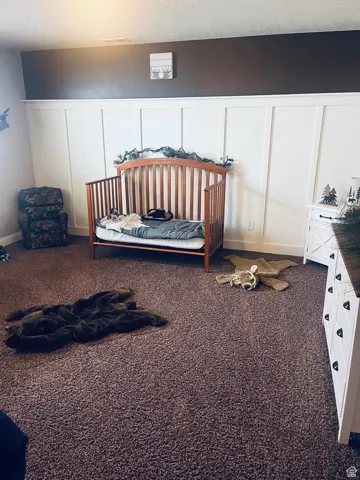 Bedroom #1 in basement featuring a decorative wall board and batten wall,  dark carpet, a textured ceiling, and a wainscoted wall