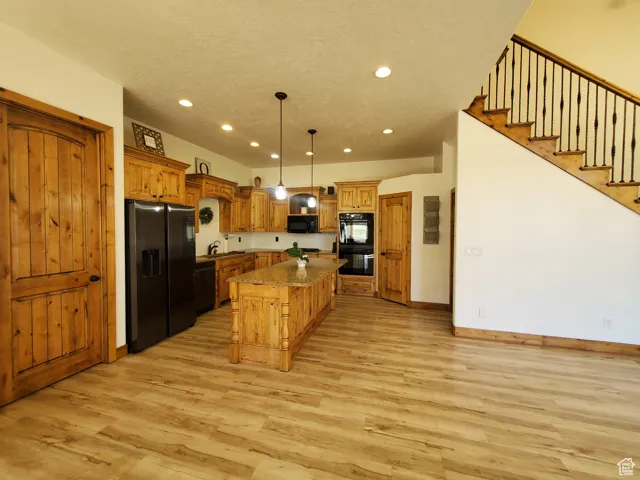 Kitchen with black appliances, decorative light fixtures, a breakfast bar, a kitchen island, and light wood-style flooring