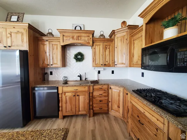 Kitchen featuring tasteful backsplash, black appliances, light wood-style floors, dark stone counters, and a textured ceiling