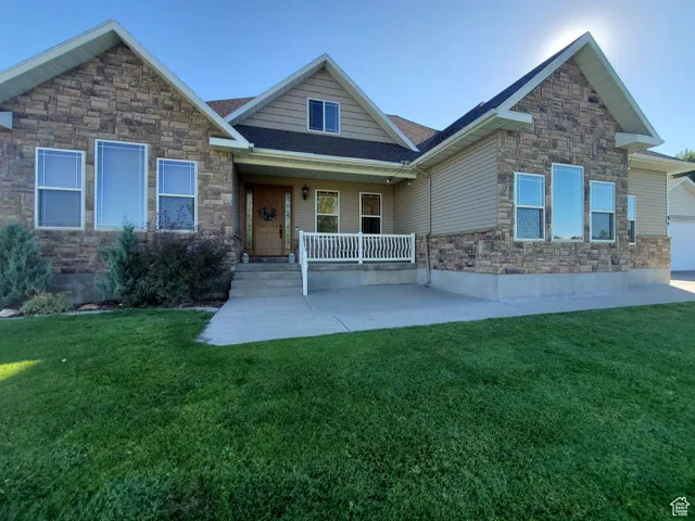 Craftsman-style house featuring covered porch, stone siding, a front lawn, and a shingled roof
