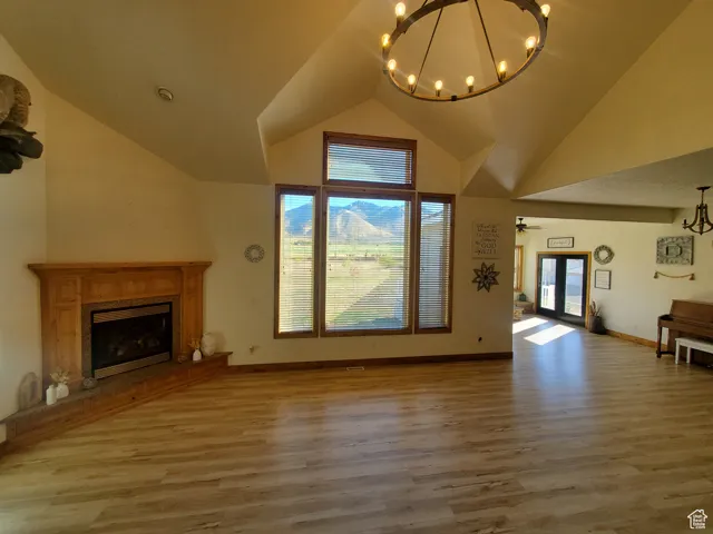 Unfurnished living room featuring light wood-style floors, a high end fireplace, a chandelier, and high vaulted ceiling