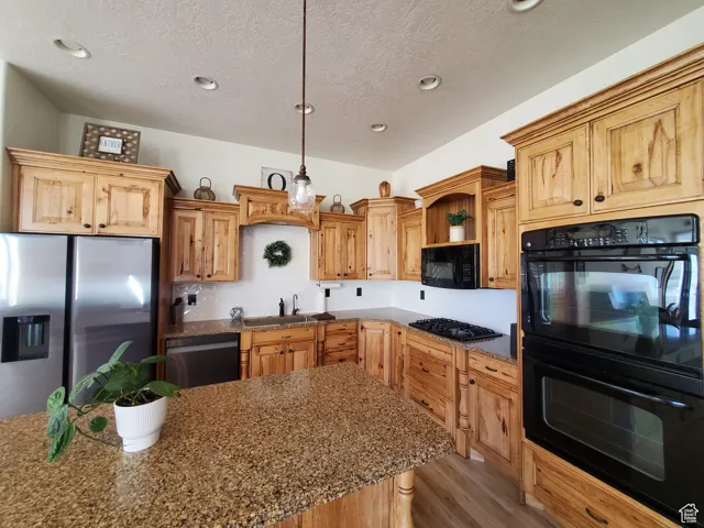 Kitchen featuring black appliances, pendant lighting, light wood-type flooring, dark stone countertops, and a textured ceiling