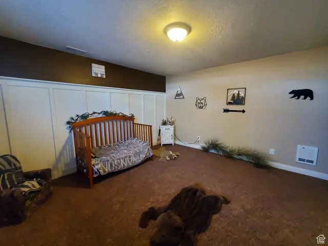 Bedroom #1 in basement featuring a textured ceiling, carpet floors, and a decorative wall