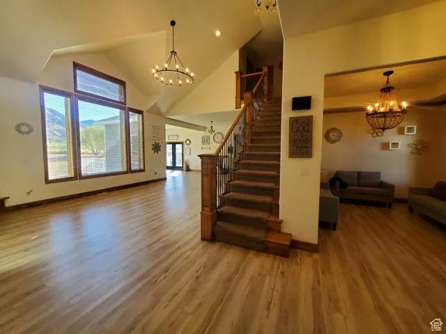 Unfurnished living room with a chandelier, high vaulted ceiling, light wood finished floors, and stairs