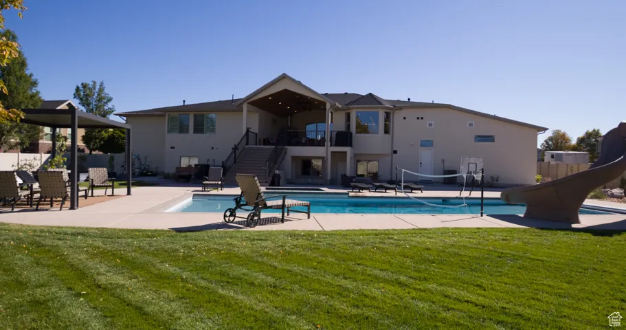 Swimming pool with stairs, a water slide, a patio area, and a balcony