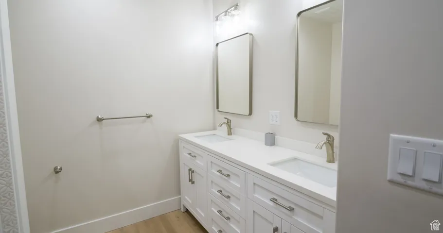 Full bath with double vanity and light wood-type flooring