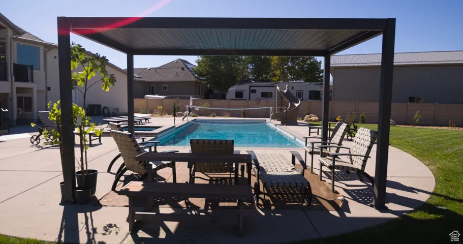 View of pool featuring a patio area, a water slide, a fenced backyard, and a pool with connected hot tub