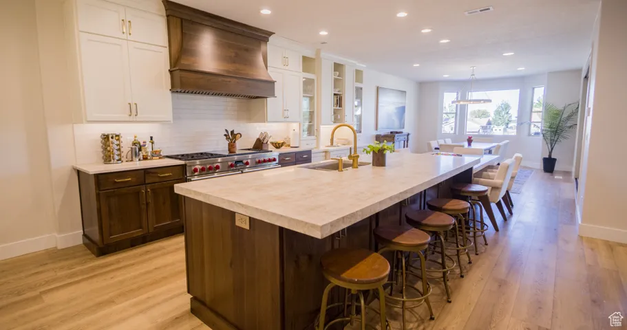 Kitchen featuring backsplash, a kitchen breakfast bar, glass insert cabinets, custom range hood, and white cabinets