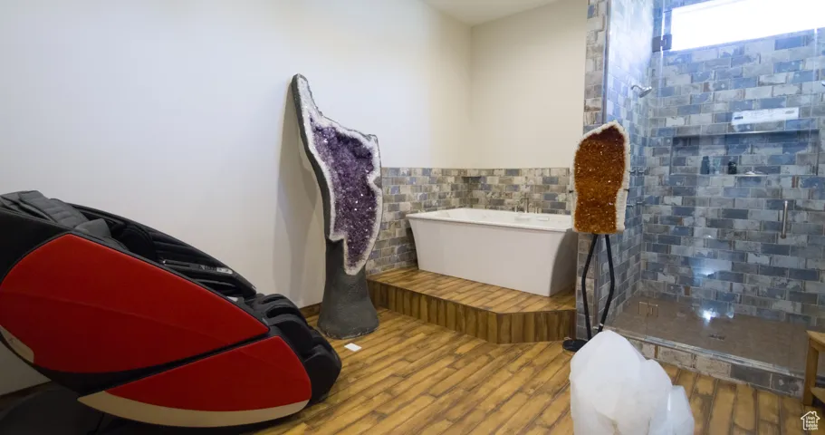 Bathroom with a soaking tub, a tile shower, wood finished floors, and tile walls
