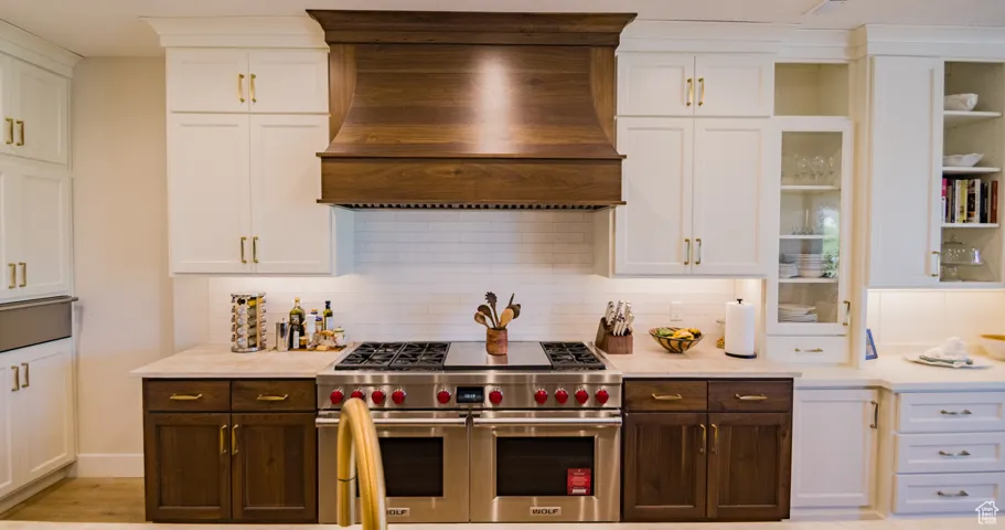 Kitchen with white cabinetry, range with two ovens, tasteful backsplash, and custom range hood