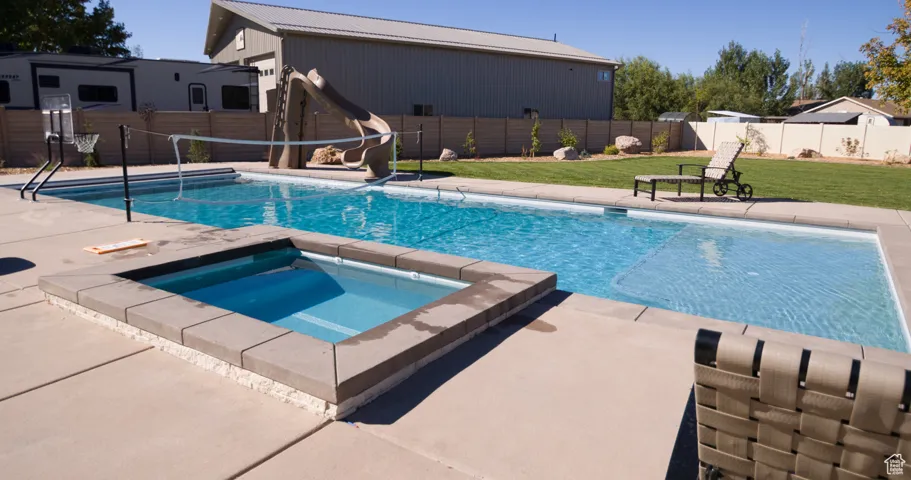 View of pool featuring a patio area, a fenced backyard, a water slide, and a pool with connected hot tub