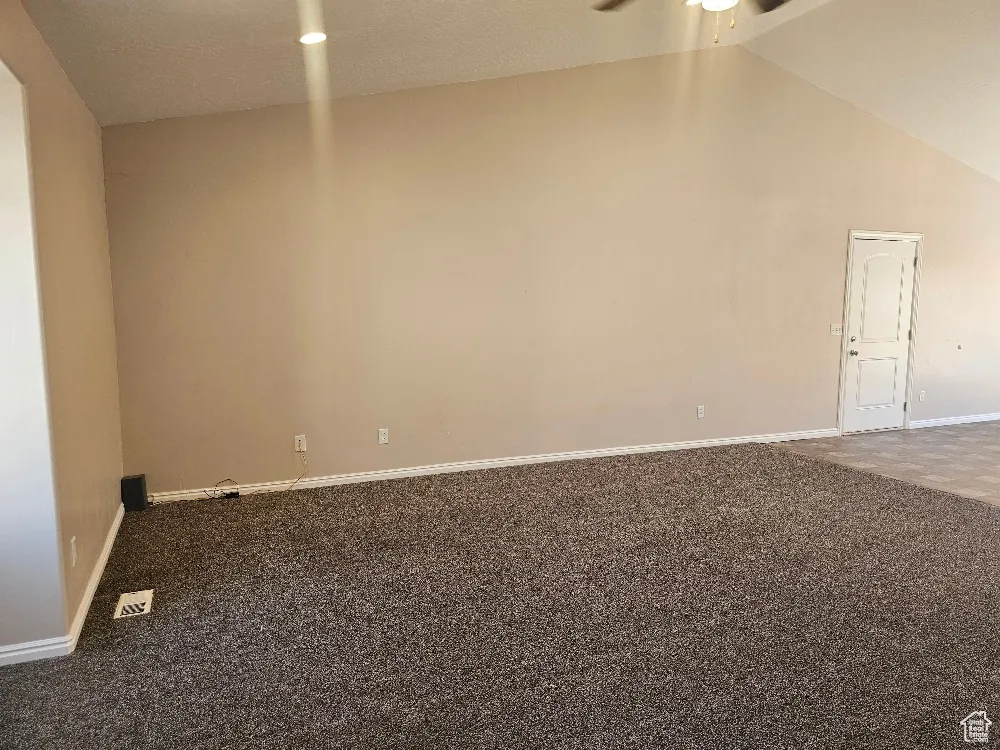 Carpeted spare room featuring a textured ceiling, high vaulted ceiling, and ceiling fan