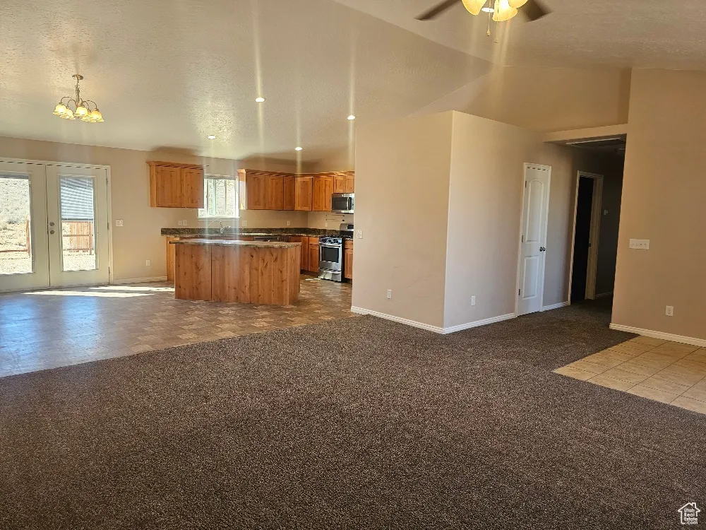 Kitchen with open floor plan, a kitchen island, dark colored carpet, brown cabinets, and vaulted ceiling