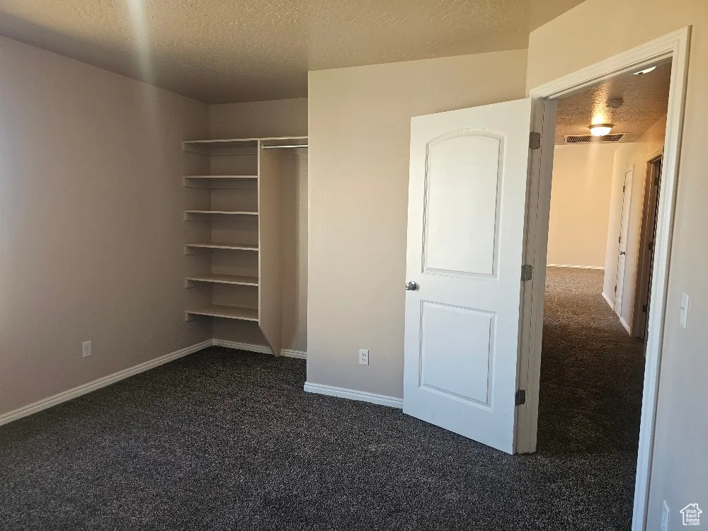 Unfurnished bedroom featuring a textured ceiling, dark carpet, and a closet