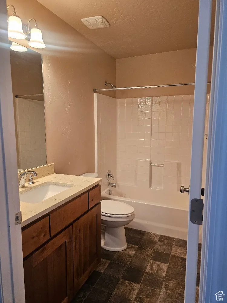 Full bath featuring bathtub / shower combination, vanity, a textured ceiling, a textured wall, and stone finish flooring