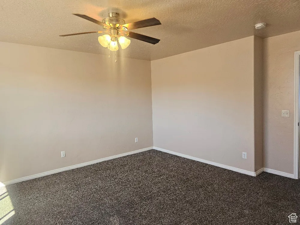 Empty bedroom room with a textured ceiling, dark colored carpet, a ceiling fan, and a smoke detector