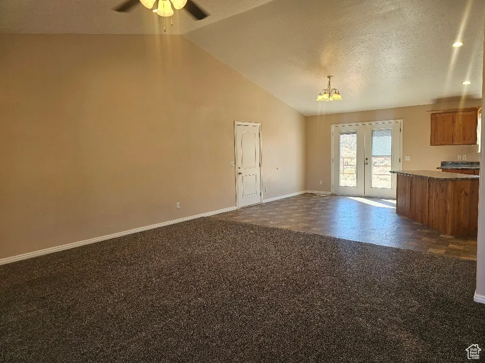 Unfurnished living room featuring a textured ceiling, vaulted ceiling, a chandelier, dark carpet, and french doors