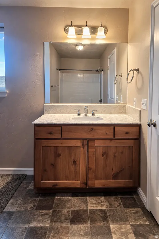 Master Bathroom Full bathroom featuring a textured wall, vanity, dark stone finish floors, and a shower