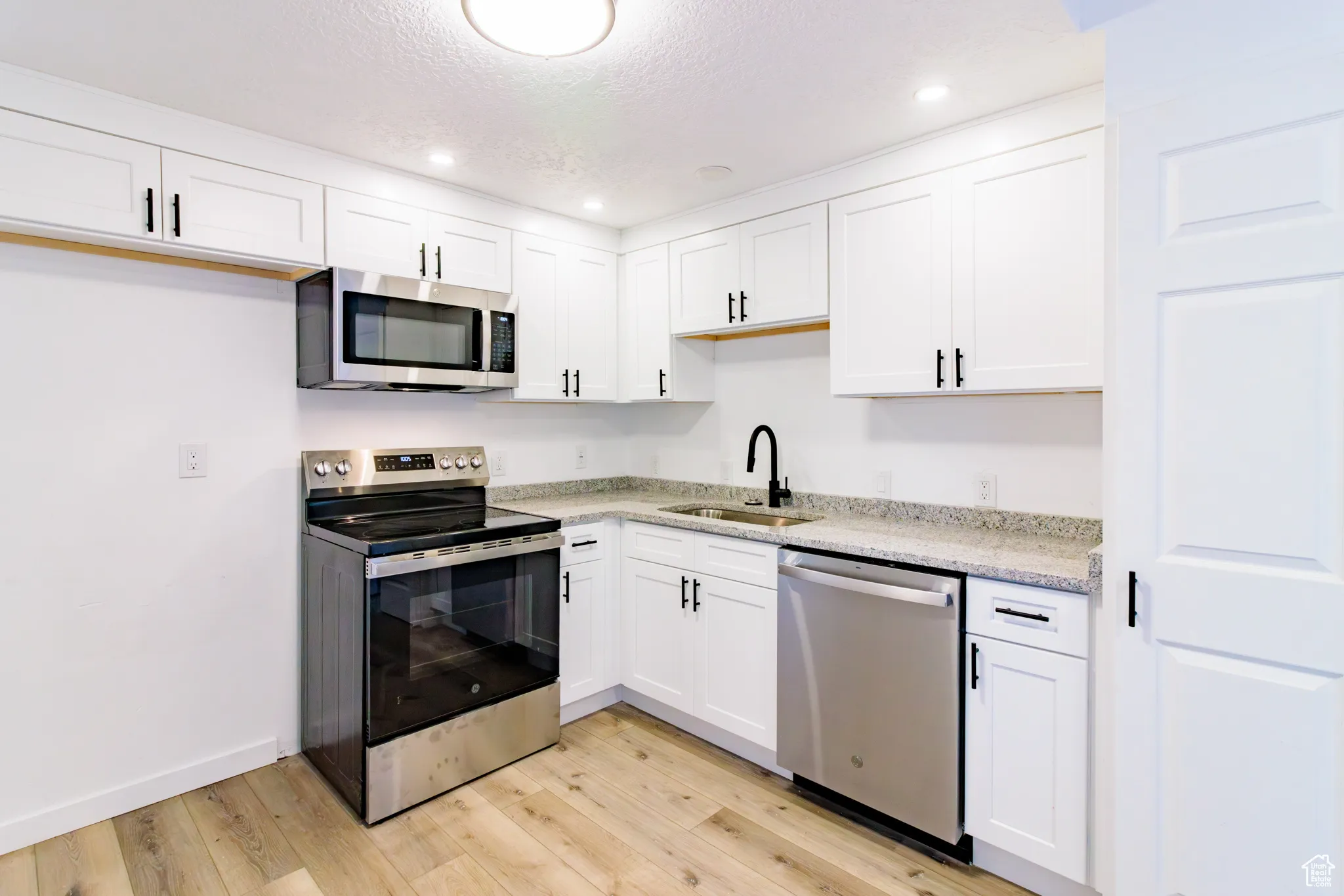 Kitchen with appliances with stainless steel finishes, white cabinets, a textured ceiling, light wood-type flooring, and recessed lighting